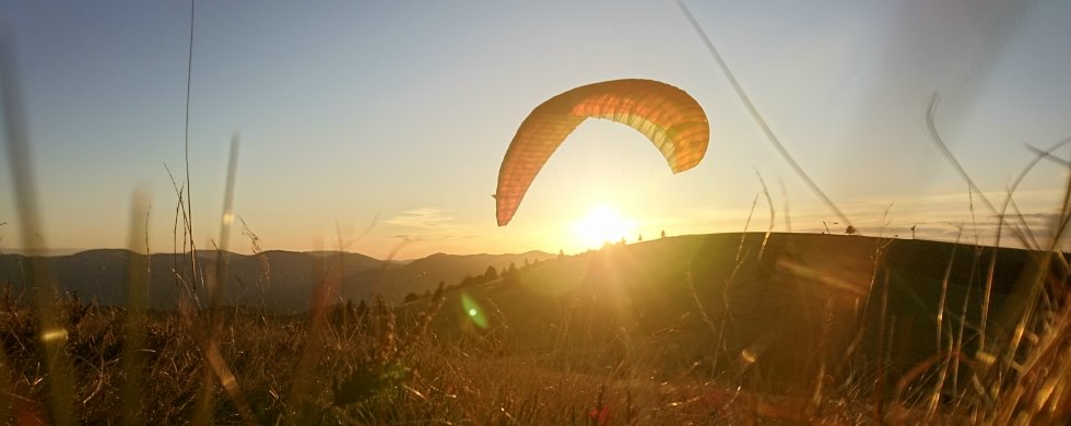 Gleitschirm im Gegenlicht über einer Bergwiese, tief stehende Abendsonne