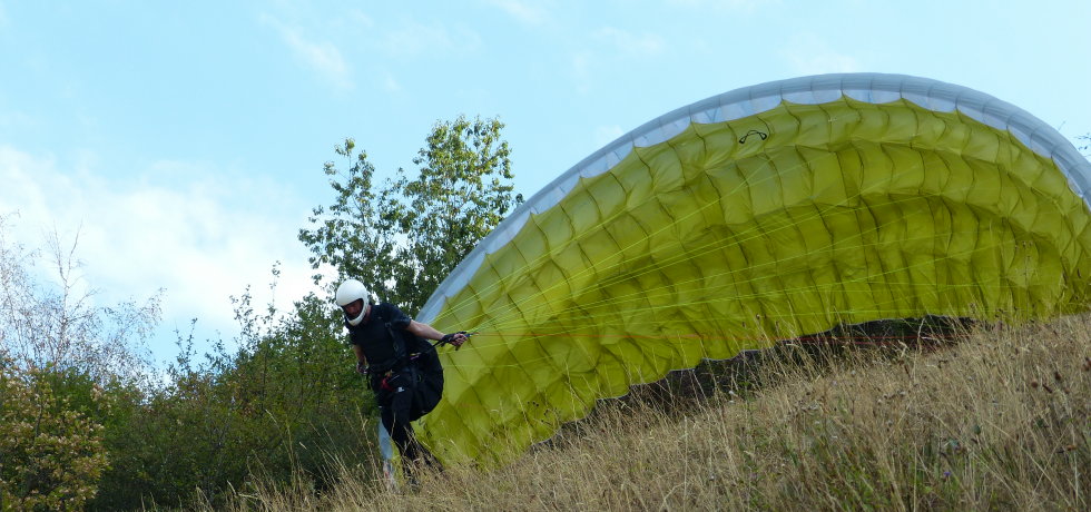 Flugschüler mit Helm zieht einen gelben Gleitschirm am Hang auf