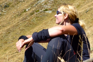 Bärbel Keinath mit Sonnenbrille, entspannt auf einem Bergabhang sitzend