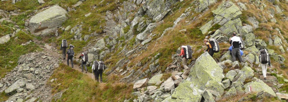 Gruppe mit großen Rucksäcken im Aufstieg über einen felsigen Bergpfad