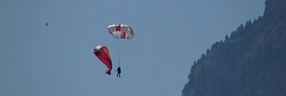 Pilot am geöffneten Rettungsschirm, der Gleitschirm hängt eingeklappt daneben